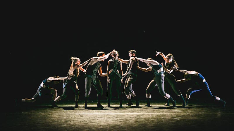 The cast stands in a straight line and attach themselves to the person standing next to them by their hands